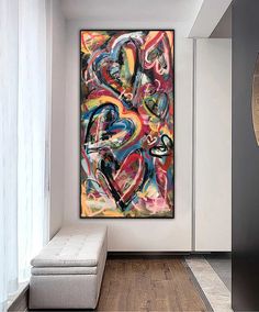 an abstract painting hangs in the corner of a room with white walls and wooden floors