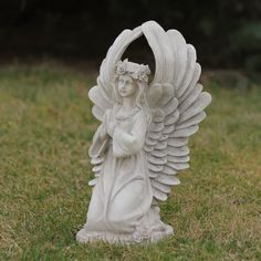 an angel statue in the grass with its wings spread out and holding a flower crown