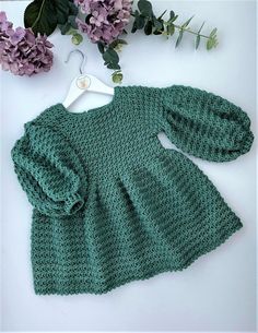 a green knitted sweater with flowers on the side and a hanger in front