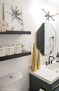 a bathroom with black and gold decor on the wall, white toilet and green cabinetry