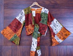 Add some boho flair to your wardrobe with this vibrant bell sleeve patchwork top. Perfect for festivals, beach outings, or everyday wear, this top is sure to make you shine. Design & Print: Celestial Print: Features an enchanting combination of suns, moons, stars, and shooting stars. Colorful Patchwork: Crafted from a unique mix of warm tones in earthy oranges, greens, red, white, blue and browns. Bell Sleeves & Crop Length: Bell Sleeves: Long, flared sleeves add a whimsical touch to the design. Crop Length: Stylish tie-front closure at the waist gives a flattering cropped look. Measurements: Bell sleeve top S/M Length: 16.5 inches Bust: 36 inches Arm Hole: 18 inches Sleeve Opening: 35 inches Sleeve Length: 22 inches Shoulder Width: 16.5 inches L/XL Length: 18.5 inches Bust: 40 inches Arm Stars Colorful, Boho Crop Top, Celestial Print, Festival Shirt, Boho Crop Tops, Patchwork Top, Festival Shirts, Hippie Festival, Shooting Star