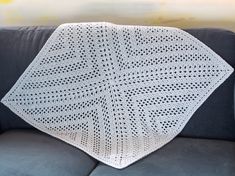 a white crocheted blanket sitting on top of a couch next to a gray sofa