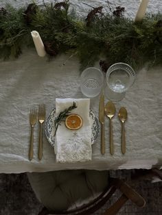 the table is set with silverware and an orange slice on it, along with pine branches