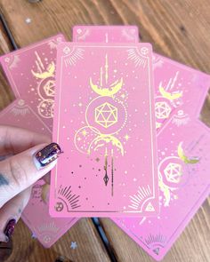 a hand holding four pink playing cards on top of a wooden table