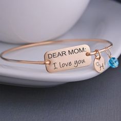 A stainless steel rectangle measuring 1 inch across is engraved with "DEAR MOM: I love you". Each bangle is hand formed from sterling silver wire, then hammered and tumbled for shine and strength. Bracelets are available in 14k gold filled and 14k rose gold filled. All charms are optional. Choose from 3/8 inch initial charms (they include the heart on them as shown) 6mm Swarovski crystal birthstone charms Note: Our bangle bracelets do not have clasps and they slide over the hand. Use the Bangle Custom Bangle, Personalised Bangle, Bracelet Size Chart, Graduation Jewelry, Rose Gold Charms, Dear Mom, Yoga Jewelry, Gold Bangle Bracelet, Birthstone Charms