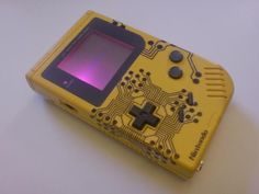 an old yellow gameboy sitting on top of a white table next to a purple light