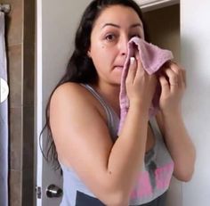 a woman wiping her face with a pink towel in front of a bathroom mirror,