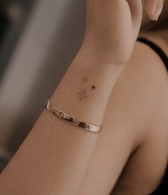 a woman wearing a gold bracelet with a star tattoo on her wrist