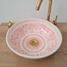 a pink and white sink sitting on top of a wooden counter next to a faucet