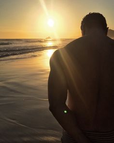 a man standing on top of a sandy beach next to the ocean at sunset or sunrise