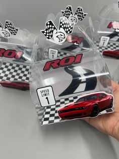 the hand is holding three red cars in plastic packaging with black and white checkered decals on them