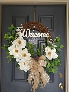 a welcome wreath with white flowers hanging on a door