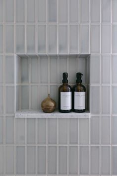 two bottles sitting on top of a white shelf in a bathroom next to a vase