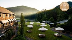 there are many tables and umbrellas in the grass near a building with mountains in the background