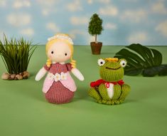 two crocheted dolls sitting next to each other on a green surface with plants in the background