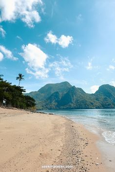 a sandy beach next to the ocean with mountains in the backgroung and blue sky