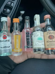 a person holding several different types of alcohol in their hand and steering wheel behind them