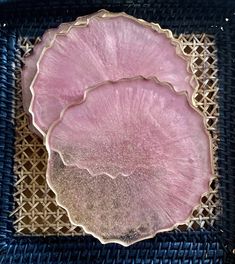 a pink and gold plate sitting on top of a blue woven place mat next to a black basket