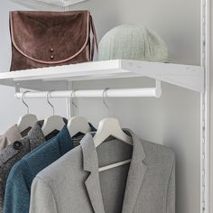 three jackets and a handbag hanging on a white shelve in a closet