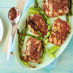 grilled fish and asparagus on a white platter with a spoon next to it