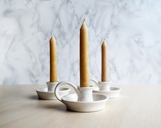 three candles sitting on top of a wooden table next to white cups and saucers