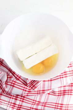 an egg and two slices of cheese in a white bowl on a red checkered cloth