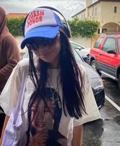 a woman with long black hair wearing a blue hat and white t - shirt in a parking lot