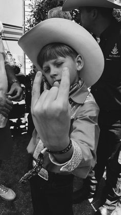 a young boy wearing a cowboy hat and holding his hand up to his face while standing next to other people