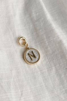 Image shows the 'N' alphabet charm against a white background. Charm is a gold circle with pearlescent center and has gold letter N in the center. Everyday Gold Pearl Charm, White Jewelry With Logo Charm As A Gift, White Jewelry With Logo Charm For Gift, White Monogram Jewelry For Everyday, Gold Initial Pendant Charms, Gold Round Pendant Charm With Pearl, Gold Monogram Charms For Gifts, Alphabet Charms, Single Letter