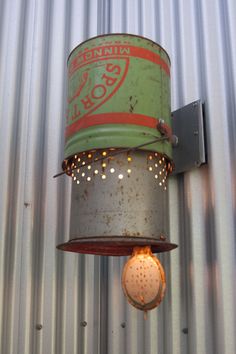 an old fashioned light hanging from the side of a building with tin cans attached to it