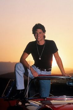 a man sitting on the hood of a car at sunset