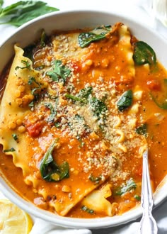 a white bowl filled with pasta and spinach covered in sauce next to lemon wedges