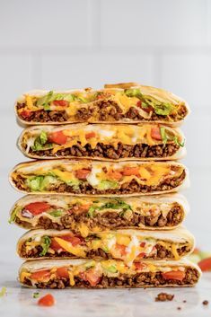 four tacos stacked on top of each other with cheese and meat in the middle