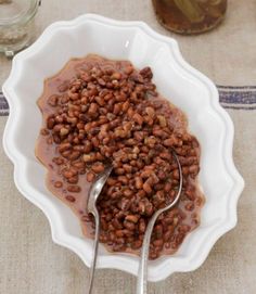 a bowl filled with beans sitting on top of a table next to two spoons