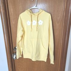 a yellow hoodie with white flowers on it hanging from a wooden door hanger