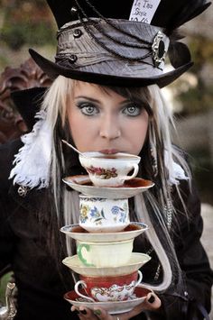 a woman wearing a top hat with tea cups in her mouth