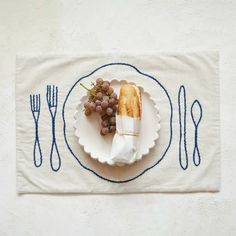 a white plate topped with bread and grapes on top of a table next to utensils