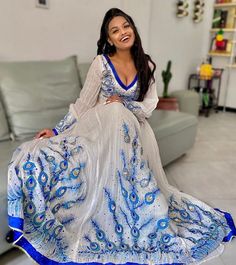 This exquisite Habesha Kemis is designed to make you feel like a true queen. Made with luxurious Menen fabric in a stunning shade of blue, the dress features intricate Tilf embroidery all over, adding a touch of traditional charm. The dress is adorned with beautiful beads that sparkle and shine in the light, adding a touch of glamour and sophistication. The bottom of the dress is made of soft and flowy Tilet fabric, which gracefully sways with every step you take. Perfect for weddings, religious Embroidered Georgette V-neck Dress, Embroidered V-neck Georgette Dresses, V-neck Georgette Dress With Mirror Work, V-neck Georgette Dress For Navratri, Eid V-neck Dress With Mirror Work, Designer Anarkali Dress With V-neck, Semi-stitched V-neck Dress For Festive Occasions, Semi-stitched V-neck Festive Dress, V-neck Designer Zari Work Dresses