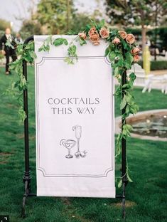 a sign that says cocktails this way with flowers and vines around it on the grass