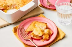 a pink plate topped with a piece of cake next to a glass of water and fork