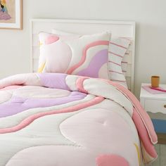 a bed with pink, purple and white comforter in a girls's bedroom