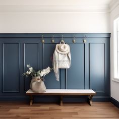 a hat, coat rack and vase with flowers on a bench in front of a blue wall