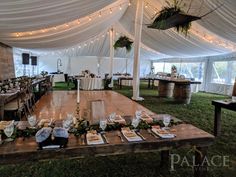 a table set up with place settings for an event in a large white tented area