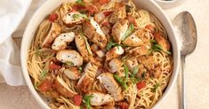 a white bowl filled with pasta and chicken on top of a table next to a spoon