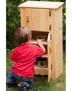 a little boy that is kneeling down in front of a wooden cabinet with the door open