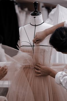 a woman is making a dress on a mannequin in front of other people