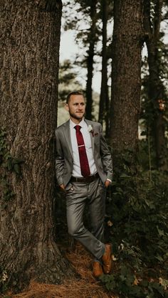 a man in a suit standing next to a tree with his hands on his hips