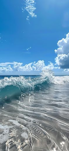 an ocean wave breaking on the beach under a blue sky with white clouds and sunbeams