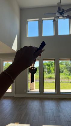 a hand holding a house key in front of a large open living room with sliding glass doors