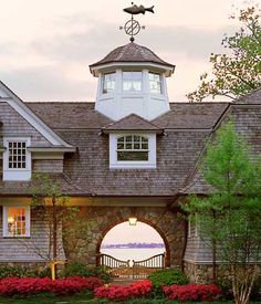 a house with a clock on the top of it's roof next to flowers and trees